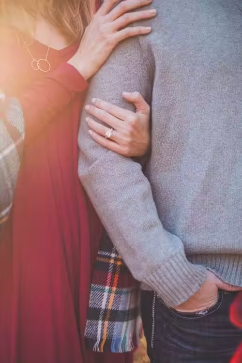 Close-up of a woman’s hand with a diamond ring on her finger, embracing a man in a gray sweater.