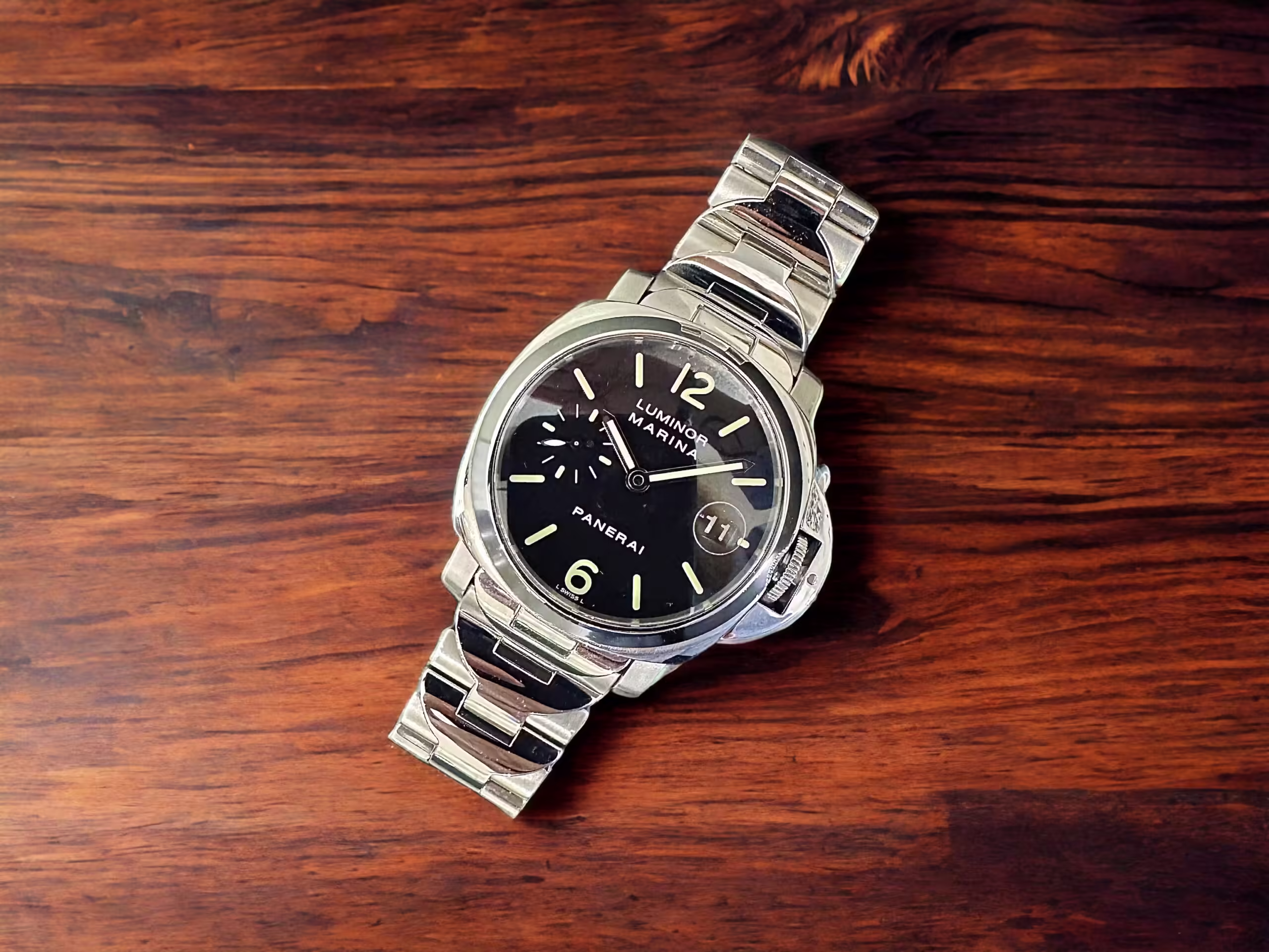 Reloj de pulsera de lujo Panerai Luminor con correa de acero inoxidable sobre madera.
